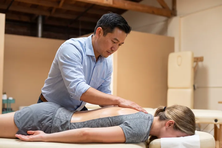 A clinician performing hands-on soft tissue work along a patient&rsquo;s back