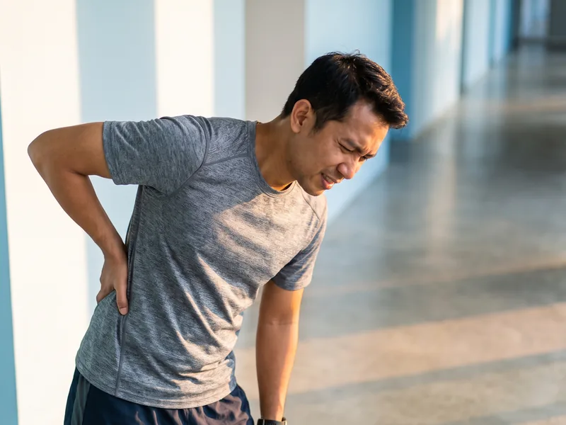 A man pausing mid-stride with his hand on his lower back